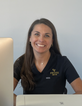 a woman sitting at a table with a laptop and smiling at the camera